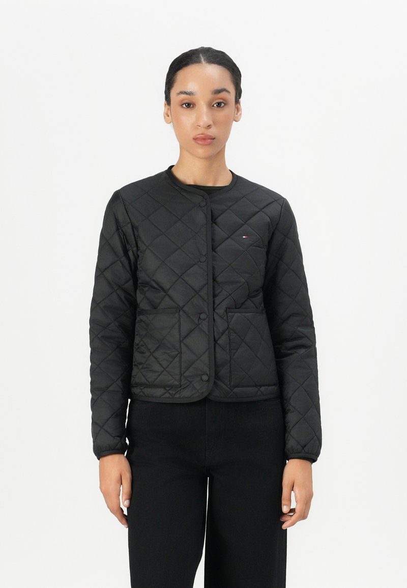 Black quilted jacket with a round neck, buttons, and two front pockets. Features a smooth texture and fitted design.