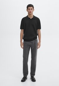 Black short-sleeve polo shirt with a soft texture, paired with faded gray jeans and black shoes. Minimalist design, no patterns.