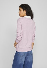 Light pink sweater with ribbed cuffs and hem, featuring a v-neck design. Paired with blue wide-leg jeans, showcasing a casual look.