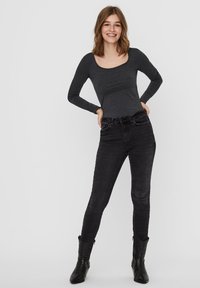 Hosszú ujjú, sötétszürke felső, kerek kivágással, fekete skinny farmerral párosítva. A modellen fekete, mintás textúrájú bokacsizma van.