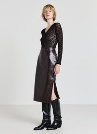 Maglietta nera a maniche lunghe con texture, abbinata a una gonna a matita in pelle lucida marrone, con uno spacco laterale, e stivali alti fino al ginocchio in pelle nera.