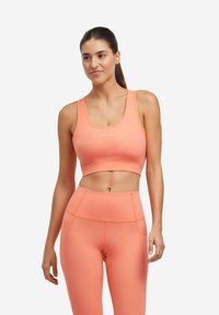 Brzoskwiniowy crop top sportowy z szerokimi ramiączkami i dopasowanym krojem, w połączeniu z legginsami o wysokim stanie z akcentowanymi szwami i ciasnym dopasowaniem.