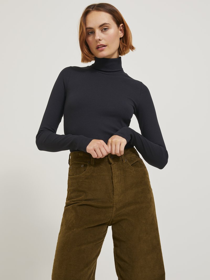 Suéter negro de cuello alto hecho de tela acanalada, combinado con pantalones de pana verde aceituna de tiro alto y textura que cuentan con bolsillos frontales.