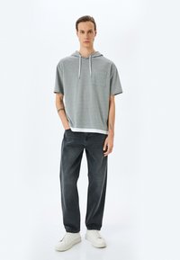 Sudadera con capucha gris de manga corta y bolsillo frontal, combinada con jeans negros y zapatillas blancas. Look limpio y casual con textura visible.