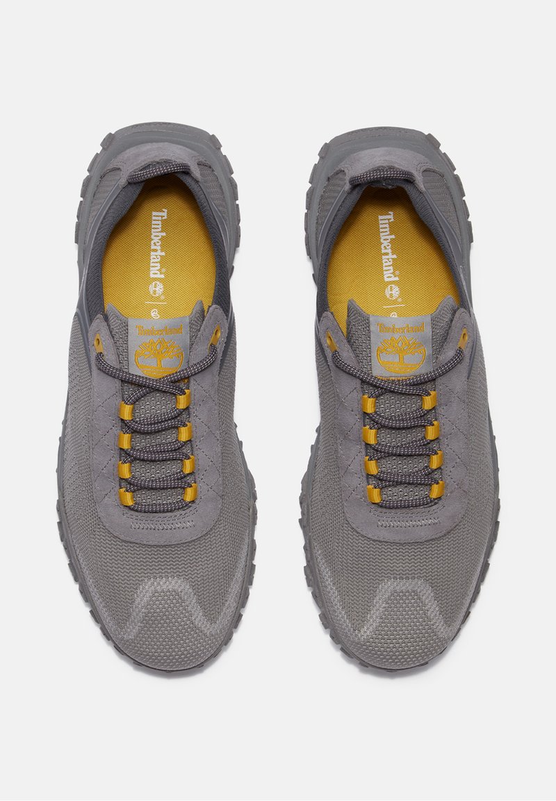 Zapatillas de malla gris con detalles amarillos, con cuello acolchado, lengüeta texturizada y suela de goma, diseñadas para ofrecer comodidad y durabilidad.
