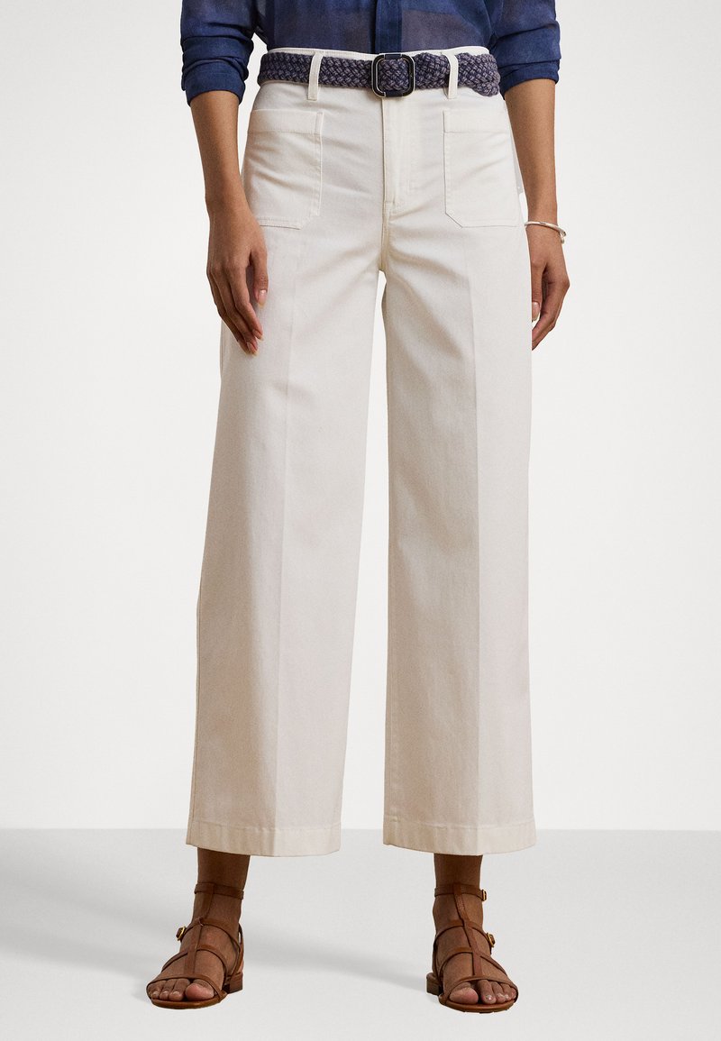 Pantalons large blancs en coton, dotés de poches avant, de passants de ceinture et d'une ceinture tressée marine, associés à des sandales brunes à lanières.
