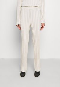 Krémové žebrované kalhoty s úzkým střihem, které mají strukturovaný pas. V kombinaci s černými botami, které zdůrazňují strukturovaný vzor látky.