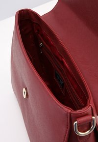 Czerwona torebka o teksturowanej powierzchni z wewnętrzną kieszenią na zamek błyskawiczny. Posiada zapięcie na magnes oraz złoty metalowy akcent. Wnętrze jest wyłożone podszewką.