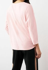 Top de manga larga color rosa claro con escote redondo y costura central en la parte posterior, combinado con pantalones negros que tienen paneles laterales beige.