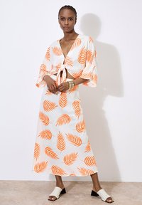 Hvid stofkjole med orange bladmønstre, som har en cropped top med bindefront og lang nederdel. Glat tekstur, afslappet pasform og brede ærmer.