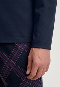 Marineblauwe longsleeve shirt met een gladde textuur, gecombineerd met gestreepte shorts in een plaidpatroon met donkerblauw, bordeauxrood en witte lijnen.