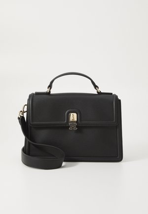 Sac à main en cuir noir avec poignée supérieure, bandoulière amovible et fermoir doré avec un logo double T sur fond blanc.