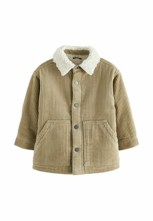 Enfant portant une veste en velours côtelé beige avec col en polaire, jean bleu retroussé et baskets montantes beiges debout sur une surface orange.