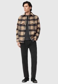 Beige ternet uldskjortejakke med mørkeblå og brune accenter, kombineret med sorte jeans og ankelstøvler, vist på en model i stående position.