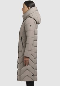 Pikk, beež puhvariidest mantel kõrge kraega, käärid musta lukuga tasku detailiga. Valmistatud õmmeldud kangast, sobib talveks.