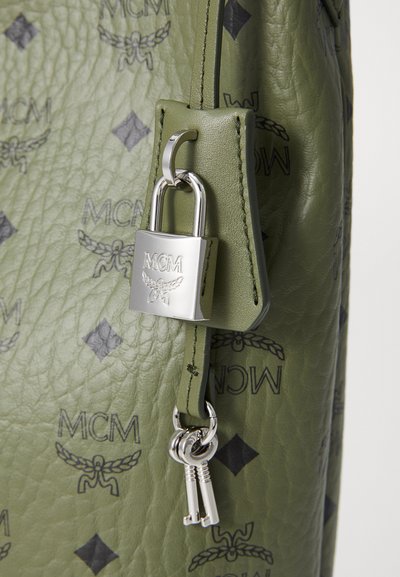 Green leather bag featuring embossed MCM logo pattern, silver lock, and key hardware accents. Textured surface with a soft finish.