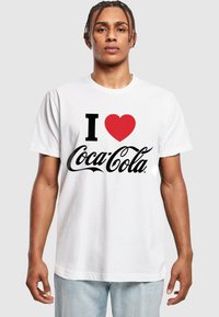 Weißes T-Shirt mit dem Grafikdesign "I ❤️ Coca-Cola" in schwarzer Schrift und rotem Herz, runder Ausschnitt, kurze Ärmel, lockerer Schnitt.