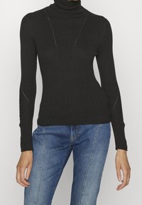 Czarny sweter z golfem i długimi rękawami, z subtelnymi szwami i dopasowanym fasonem. W połączeniu z niebieskimi dżinsami.