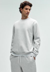 Helehall sweatshirt ümmarguse kaelusega, pikkade varrukatega ja soonikkäärtega. Pehme tekstuur, koos sobivate helesiniste sviitritega.