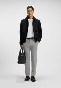 Giacca bomber nera con due tasche frontali, maglione bianco a maglia, pantaloni grigio chiaro, cintura nera, borsa nera, scarpe nere.