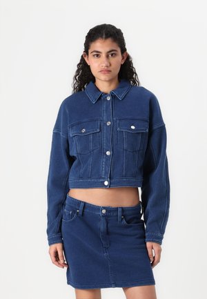 Denim crop jacket in dark blue with a buttoned front, two chest pockets, and contrasting stitching, paired with a matching denim skirt.