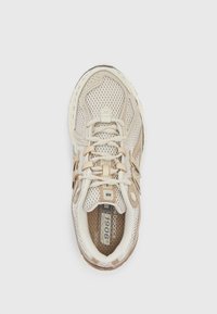 Chaussure de sport beige en mesh avec des accents marron clair. Dotée d'un design à lacets, d'un col rembourré et d'une semelle en caoutchouc avec une prise texturée.