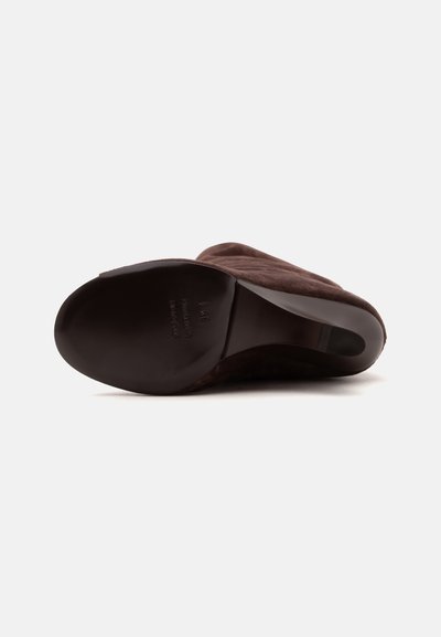 Chaussure en daim marron à petit talon montrée par en dessous, mettant en valeur la semelle lisse et la forme arrondie du bout.