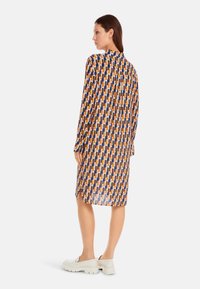 Langarmkleid mit einem mehrfarbigen geometrischen Muster in Blau, Orange und Creme. Hergestellt aus leichtem Stoff mit einem leicht lockeren Schnitt.