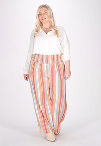Biała koszula z guzikami zestawiona z szerokimi spodniami w multikolorowe paski, posiadającymi elastyczną talię. Obuwie w kolorze beżowym. Prosty, casualowy design.