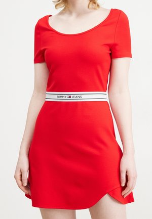 Mujer que lleva un vestido corto rojo con mangas cortas y una cintura blanca con la etiqueta Tommy Jeans.