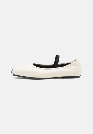 Flat ballet shoe in white leather with a rounded toe, black elastic strap, and small gold emblem near the heel. Soft texture and minimalist design.