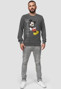 Šedá mikina s barevným grafickým motivem Mickey Mouse a textem. Materiál vypadá měkký, má dlouhé rukávy a kulatý výstřih.
