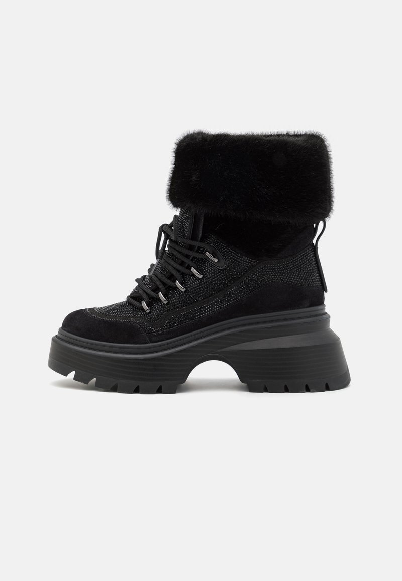 Bottine noire à plateforme à lacets avec semelle épaisse texturée et revers en fausse fourrure plié sur fond blanc.