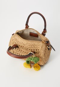 Woven straw torba s smeškanom od smeđeg kože i zlatnim zatvaračem, koja sadrži šareni pom-pom privjesak s zelenim listovima i žutim cvjetovima.
