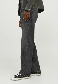 Mustad denim püksid vabalt istuva lõikega, nähtava õmblusega ja räbaldunud ääred, koos mustade spordijalatsitega, millel on valged tallad ja paelad.