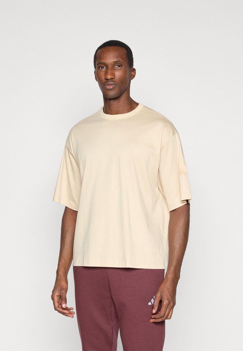 Béžové oversized tričko vyrobené z mäkkého materiálu, s okrúhlym výstrihom a krátkymi rukávmi. Kombinované s vínovými teplákmi s logom.