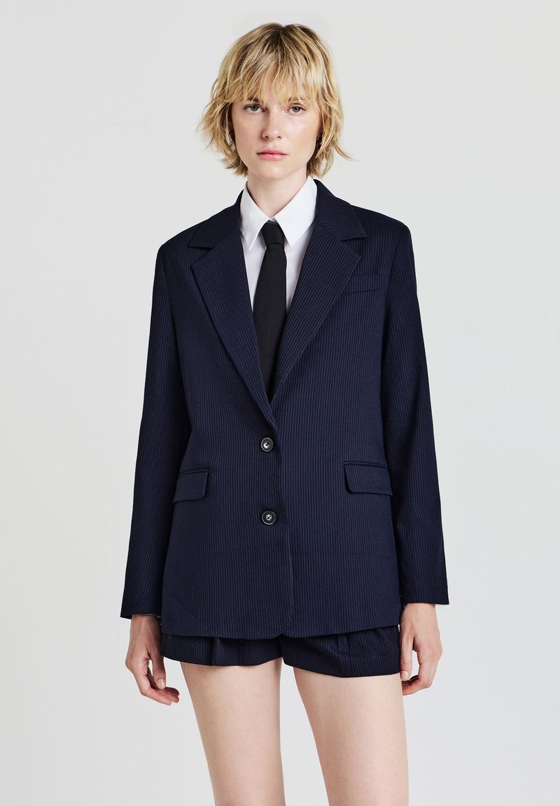 Blazer oversize à rayures marines avec deux boutons, revers crantés et poches latérales, associé à un short taillé assorti.