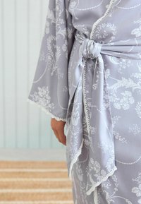 Robe grigio chiaro con un motivo floreale bianco, maniche lunghe e una cintura in vita. Presenta un bordo in pizzo lungo i bordi e una texture morbida e liscia.