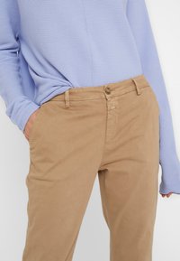 Světle modrý žebrovaný top s dlouhým rukávem v kombinaci s béžovými bavlněnými chinos kalhotami. Chinos mají přední zapínání na knoflík a postranní kapsy.