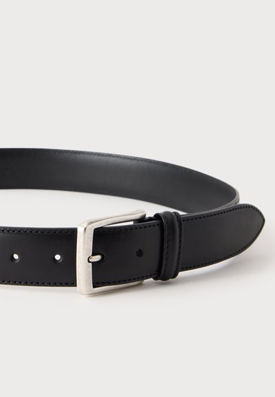 Ceinture en cuir noir avec boucle métallique rectangulaire argentée posée à plat sur une surface blanche.