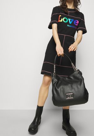 Black dress with colorful "Love Moschino" logo, pink stitching detail, paired with a large black textured handbag and black ankle boots.