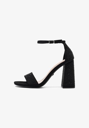 Fekete szandál velúr hatással, boka pánttal, széles tömbsarokkal, amelyet apró szegecsek díszítenek, és téglalap alakú toe pánttal.