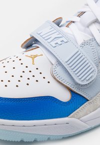 Baskets Nike Air Jordan blanches et bleues avec logo Jumpman doré, bout perforé et bride gris clair avec logo Nike en relief.