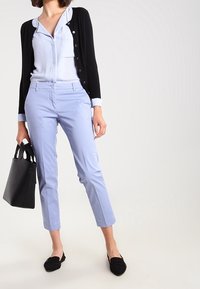 Ljusblå skräddarsydda byxor med smal passform, kombinerade med en svart cardigan. Accessoarer inkluderar en svart tygväska och svarta ballerinaskor.