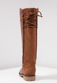 Brązowe kozaki sięgające do kolan wykonane z gładkiej skóry z zamszowym wykończeniem. Posiadają sznurowadła z tyłu, zaokrąglony nosek oraz gumową podeszwę.