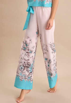 Białe spodnie z szerokimi nogawkami z niebieskimi kwiatowymi wzorami i jednolitymi niebieskimi lamówkami noszone boso, zestawione z dopasowaną niebieską kwiatową bluzką.