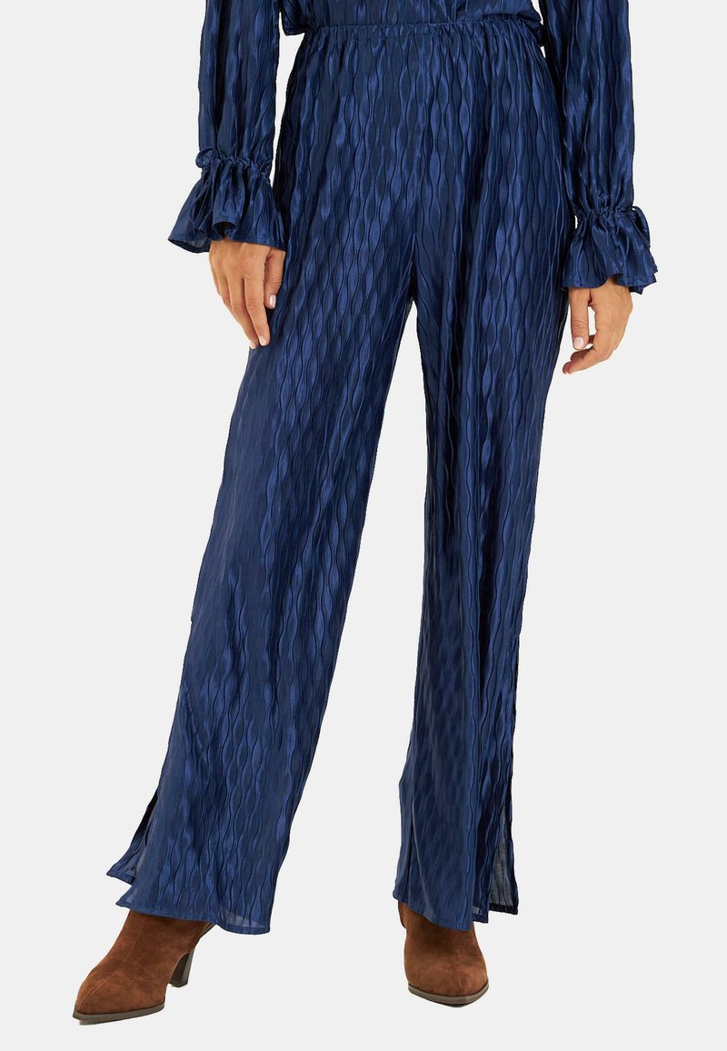 Granatowe, plisowane spodnie o szerokich nogawkach z elastyczną talią i rozkloszowanymi mankietami. Materiał ma teksturowany, falisty wzór.