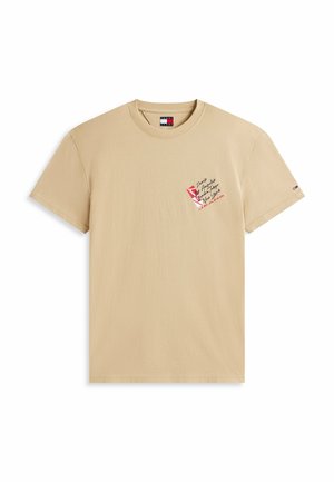 T-shirt beige à manches courtes avec col rond, petit texte graphique rouge et noir sur la poitrine gauche et petit logo drapeau sur la manche gauche.