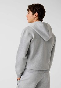 Sweat à capuche gris avec une texture douce, des poignets et un ourlet côtelés. Comprend une poche kangourou et un design simple.