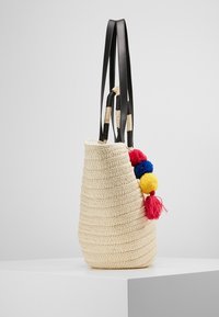 Wiklinowa torba typu tote z czarnymi skórzanymi akcentami, zdobiona kolorowymi pomponami w odcieniach czerwieni, niebieskiego i żółtego. Uformowana w strukturalny, stożkowaty kształt.